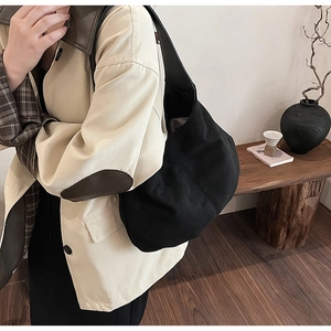 Hobo style black canvas tote bag shown worn by a model in a minimalist setting