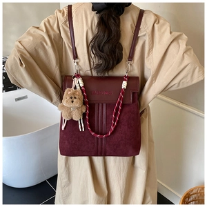 Detail of burgundy leather backpack with embossed text and plush bear charm
