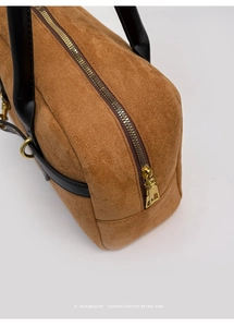Detailed close-up of brown suede Boston bag with black leather handle and gold hardware