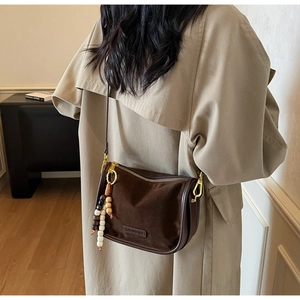 Detail of suede crossbody bag with vintage beads and golden hardware on beige coat