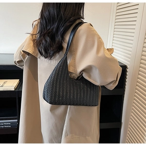 Dettaglio della borsa a spalla intrecciata nera indossata con un trench coat beige