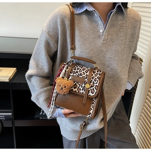 Detail of leopard print crossbody bag with bear charm and scarf on a model