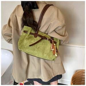 Detail of green suede tote bag featuring brown leather straps and wooden bead charm