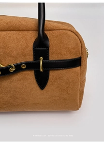 Detailed close-up of brown suede Boston bag with black leather straps and gold metal buckles