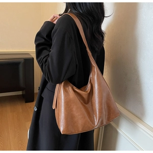 Brown PU leather tote bag shown from side view on model wearing a black coat