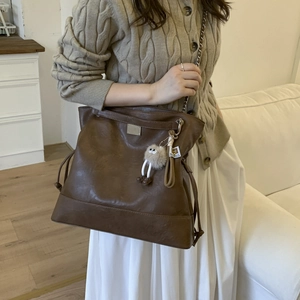 Détail du sac vintage en similicuir marron avec bandoulière chaîne et pompon décoratif