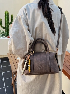 Vintage dark brown Boston bag with embossed text and colorful wooden bead charm detail