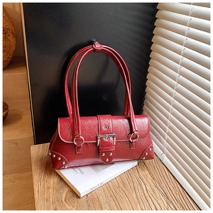 Close-up of red vintage rivet pillow bag with silver buckles on a wooden table