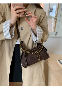Detail of dark brown quilted crossbody bag with gold chain strap on model in trench coat