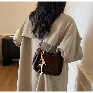Détail du sac demi-lune marron mat avec perles en bois porté sur un trench-coat beige