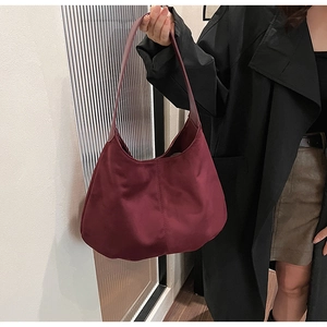 Detail view of burgundy nylon hobo shoulder bag held by a model for a chic fall look