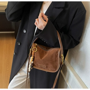 Détail du sac en daim marron avec pendentif en perles de bois et plaque logo métallique