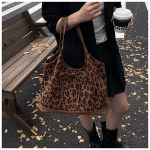 Outdoor street view of a large leopard print tote bag with brown leather handles and bow