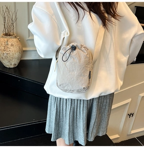 Close-up of beige drawstring phone bag with woven strap worn by a model in casual style