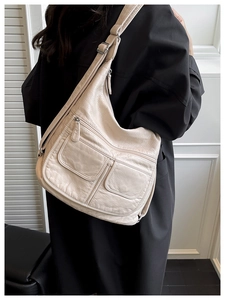 Detail shot of beige soft leather multi-pocket shoulder bag on black coat with wide strap
