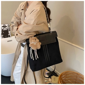 Black canvas and leather backpack detail with brown plush bear charm and woven straps