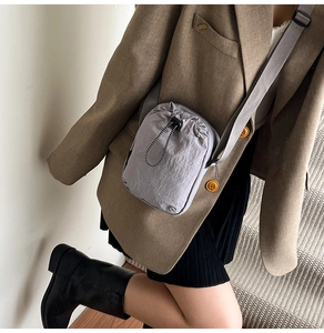 Adjustable grey drawstring crossbody bag worn by model over a brown blazer