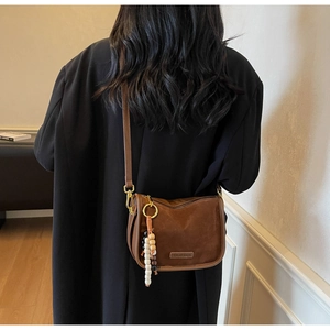 Detail of a brown suede crossbody bag featuring unique beaded tassels on a female model