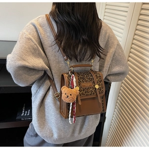 Fashionable leopard print backpack featuring brown leather detail and a plush bear charm