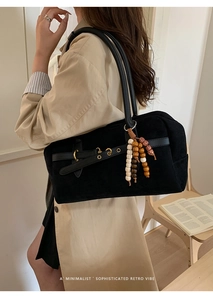 Detail of black suede shoulder bag featuring decorative wooden beads and gold hardware