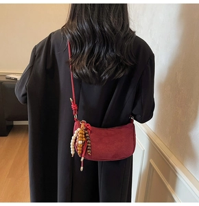 Detail of dark red crescent bag with wooden bead charm on a black wool coat