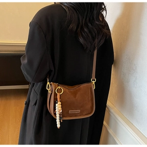 Gros plan d'un sac selle en daim marron avec pendentif en perles et étiquette