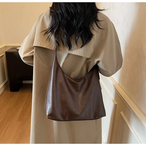 Rear view of a dark brown oil wax leather crescent shoulder bag worn on a beige outfit