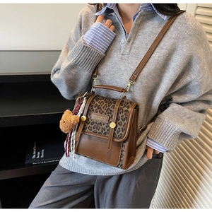 Detail of a brown leather shoulder bag with leopard print and a cute bear charm
