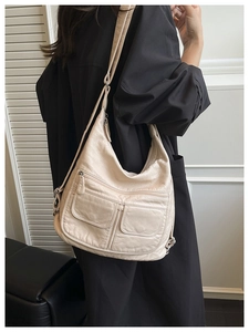 Model wearing a large cream faux leather hobo bag with multiple zipper pockets and shoulder strap