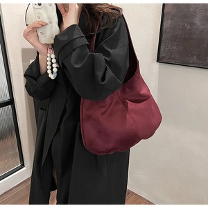 Detail of burgundy satin nylon shoulder bag worn by model over a black coat