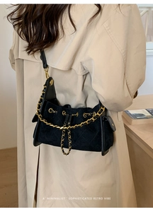 Close-up of black quilted suede shoulder bag featuring a chunky gold chain and retro design