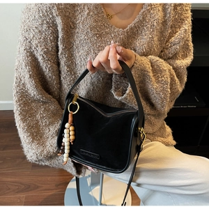 Détail d'un sac bandoulière noir givré avec breloque en perles de bois et métal doré
