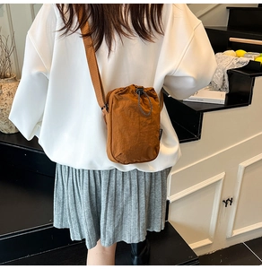 Detail of a brown nylon crossbody phone bag with drawstring closure and wide woven strap
