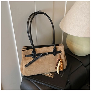 Detailed texture of brown suede tote bag with black leather straps and wooden bead charm