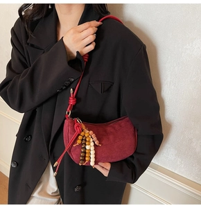 Detail of burgundy suede dumpling bag with wooden bead charm and thin strap