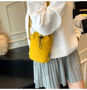 Detail of yellow nylon crossbody bag with black drawstring closure and fashion label