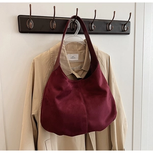 Close-up of a burgundy faux suede moon tote bag hanging on a dark wooden wall hook