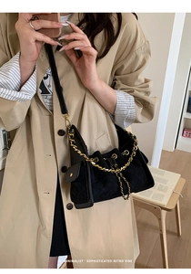 Detail of black quilted shoulder bag with gold chain strap worn with a khaki trench coat