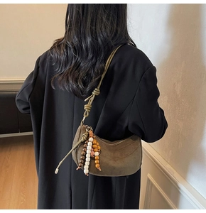 Detail of a dark brown suede crescent shoulder bag with a decorative wooden bead tassel