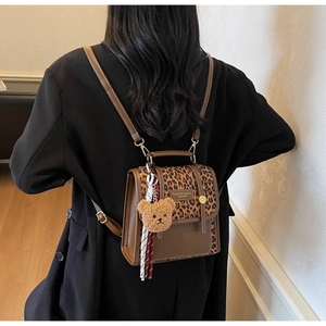 Chic brown PU leather backpack with leopard print flap and plush bear charm on a model