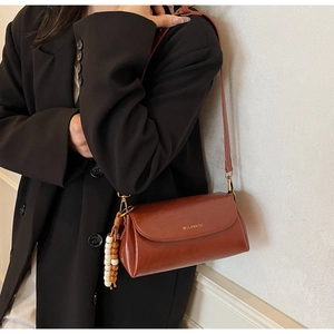 Detail of red-brown retro pillow bag with wide strap and beaded tassel on a black blazer