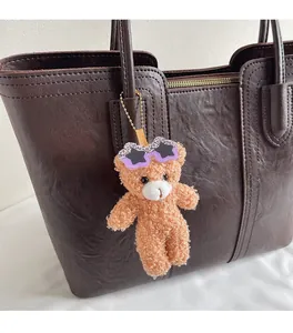 Detail of a fluffy brown bear charm with purple star sunglasses on a leather tote bag