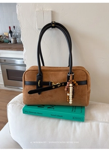 Brown suede Boston bag with black handles and vintage beads on an art book