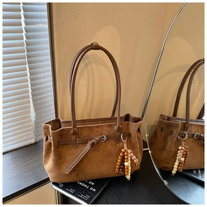 Detail of vintage brown suede tote bag with beaded tassel charm and leather buckle strap