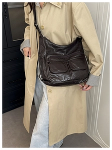 Detail of dark brown lychee leather crossbody bag with front snap pockets on beige trench coat