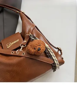 Détail du sac vintage en similicuir marron avec breloque ours en peluche et logo en métal