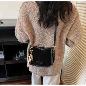 Rear view of a black suede crossbody bag with wood bead charm on a model in a cozy room