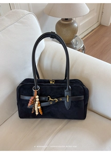 Detail of black suede Boston bag with leather straps and decorative beaded charm