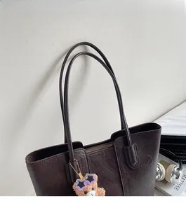 Detail of dark brown tote bag with pebble texture and cute plush bear charm
