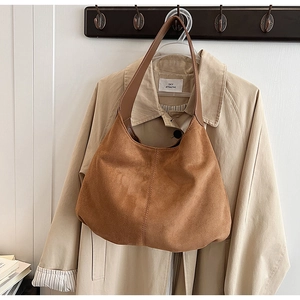 Close-up of brown suede hobo bag with leather strap hanging on a beige trench coat